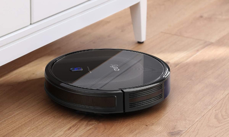the eufy BoostIQ RoboVac 11S MAX robot vacuum is running on a hardwood floor and about to clean under a cabinet. 