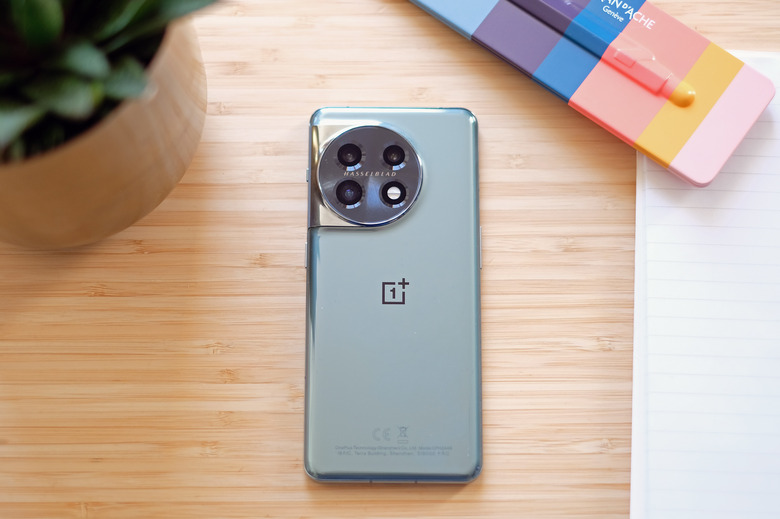 OnePlus 11 green smartphone on a table with a notepad, pen case and plant.