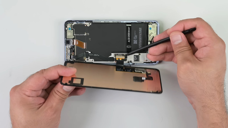 Still from an iFixit repair video of a person's hands holding a tool as they pry the front panel off the Google Pixel 8 Pro.