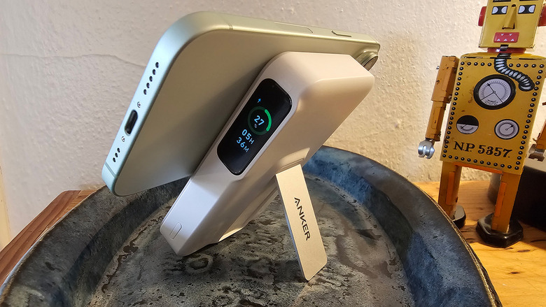 The Anker MagGo 10K battery charges an iPhone and is propped up on the kickstand. There's a yellow toy robot in the background. 
