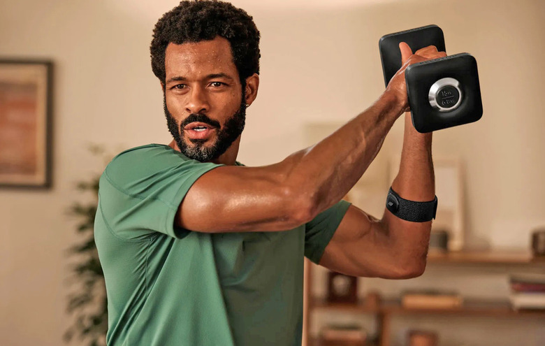 A man holds up a dumb bell during a workout in his living room.