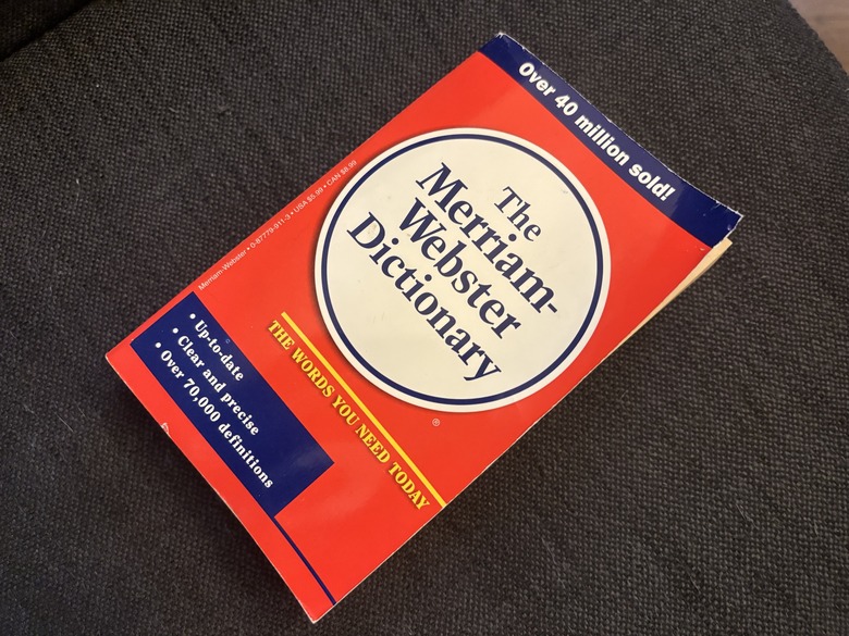 A paperback copy of a red and blue Merriam-Webster Dictionary on a navy blue background.
