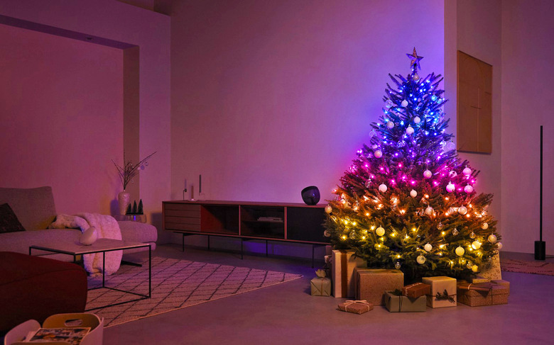 A living room is seen at night with a christmas tree lit up in rainbow tiers by the Philips Hue string lights.
