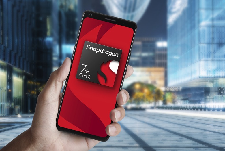 A render of a Snapdragon 7+ Gen 2 chipset displayed on a phone that someone is holding up against a a blurry, modern urban environment.