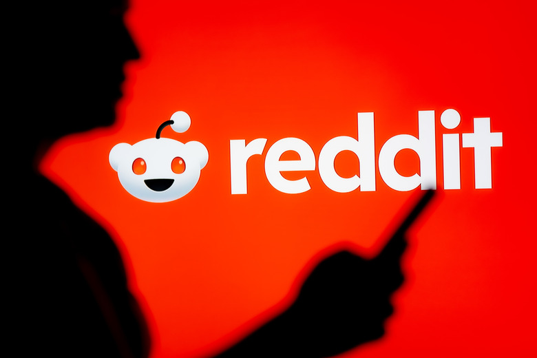 POLAND - 2025/03/07: In this photo illustration, a woman seen looking at a smartphone with a Reddit logo displayed in the background. (Photo Illustration by Mateusz Slodkowski/SOPA Images/LightRocket via Getty Images)