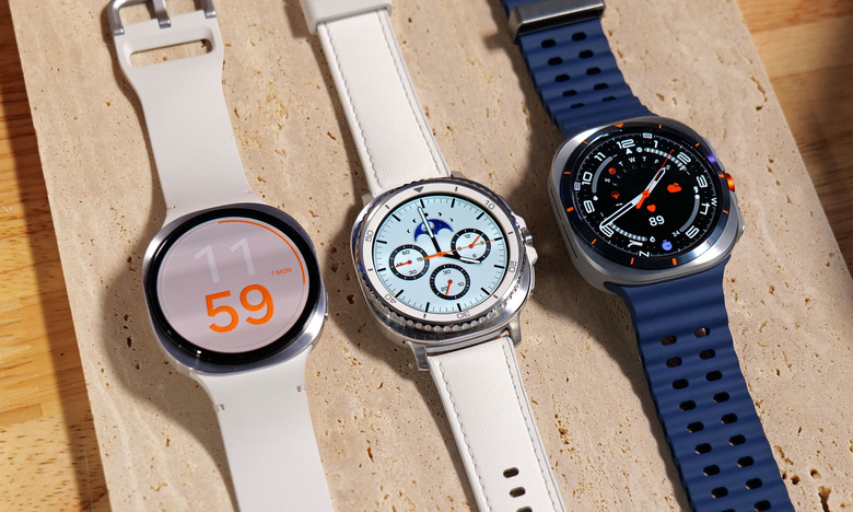The Samsung Galaxy Watch 8, Galaxy Watch 8 Classic and Galaxy Ultra (Titanium Blue model) laid out on a wooden surface.