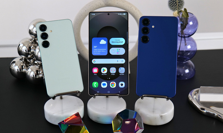 Two Galaxy S25 handsets flanking a Galaxy S25 Ultra, with their backs facing out. Each device is on a stand, and the middle device has its display facing front.