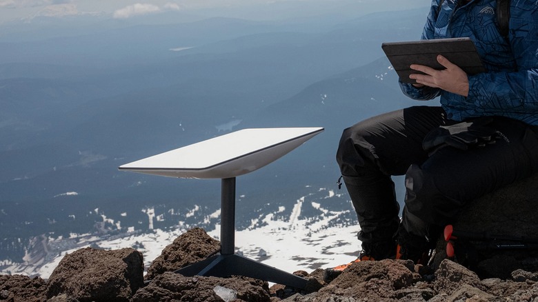 A person using a tablet next to a Starlink dish.