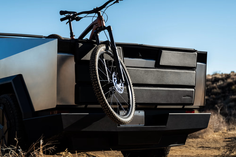 The rear end of a truck with a bike hanging out of it. 
