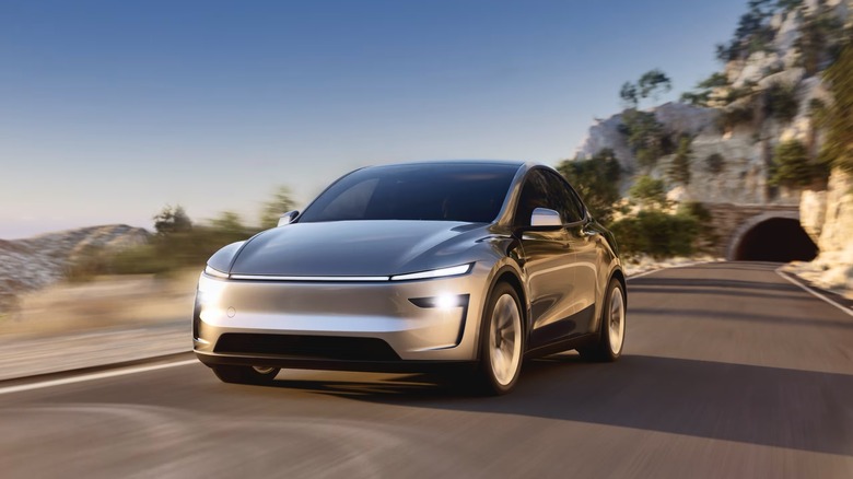 A silver Tesla Model Y driving down a mountain highway.