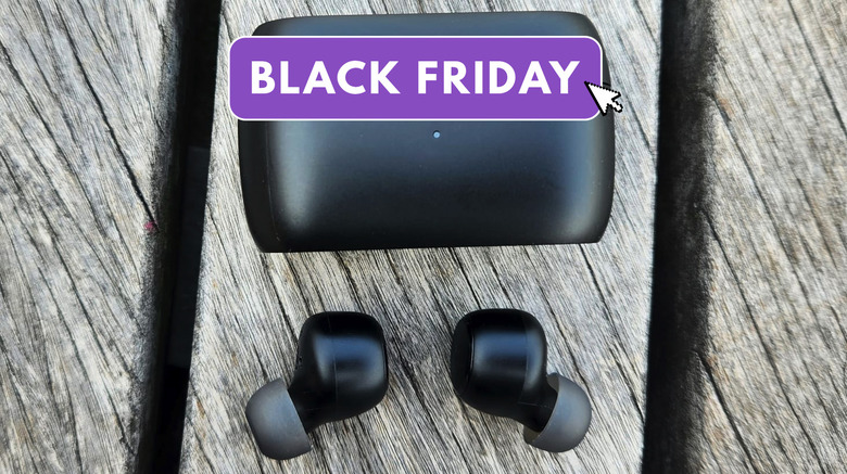 Earbuds with the black friday logo on top sit on a wooden table. 