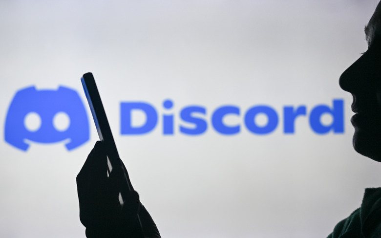 EDMONTON, CANADA - APRIL 28:
An image of a woman holding a cell phone in front of the Discord logo displayed on a computer screen, on April 29, 2024, in Edmonton, Canada. (Photo by Artur Widak/NurPhoto via Getty Images)