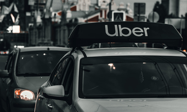Monochrome photo of traffic in an urban area. Closeup on a car with an Uber sign on top.