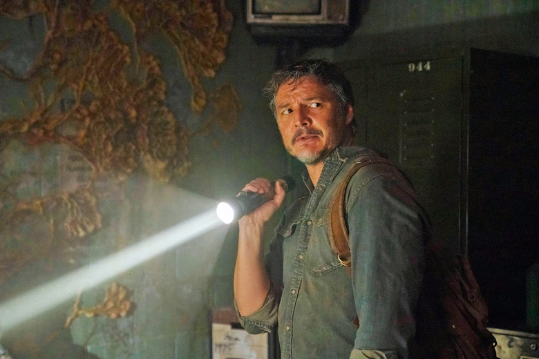 Pedro Pascal as Joel in HBO's 'The Last of Us' stands in a dimly lit room while holding a flashlight to look around.