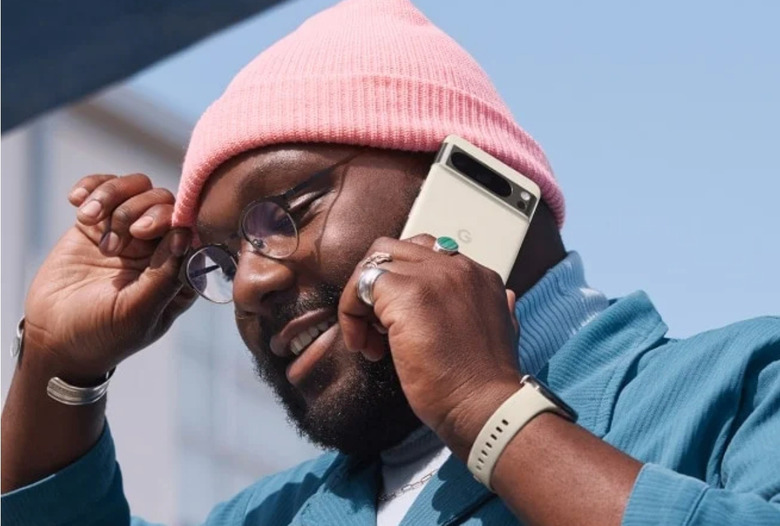 A man wearing a pink beanie and a blue blazer holding a porcelain-colored smartphone against his ear.