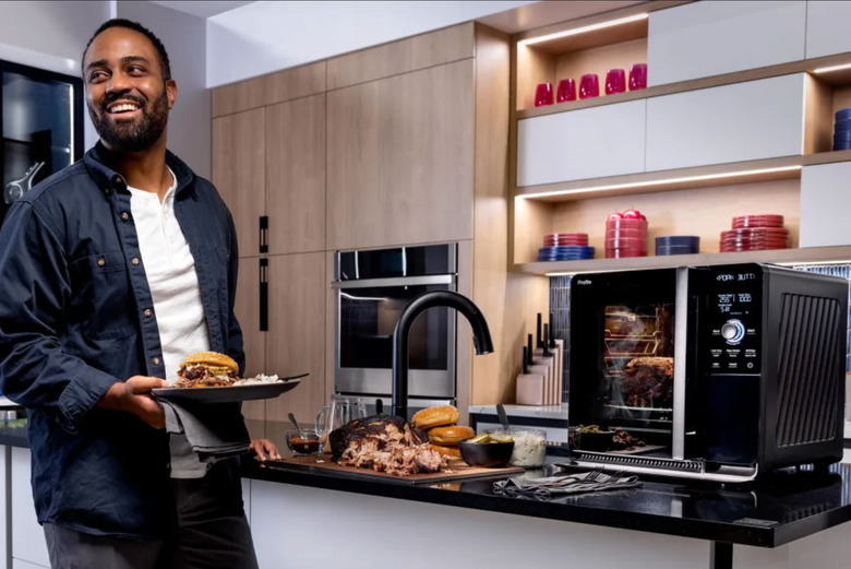 A man enjoying some smoked meat as the smoker sits beside him. 