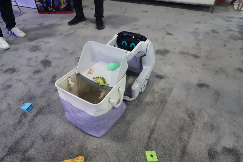 A robot with a dust pan like appendage dumps toys into a bin.