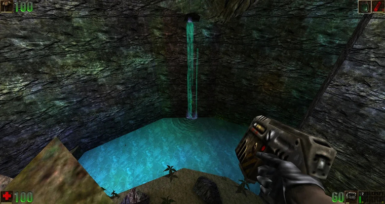 A screenshot from Unreal, showing a waterfall and a small lake at the bottom of a cliff. The player-character is shown from a first-person perspective and is holding a pistol.