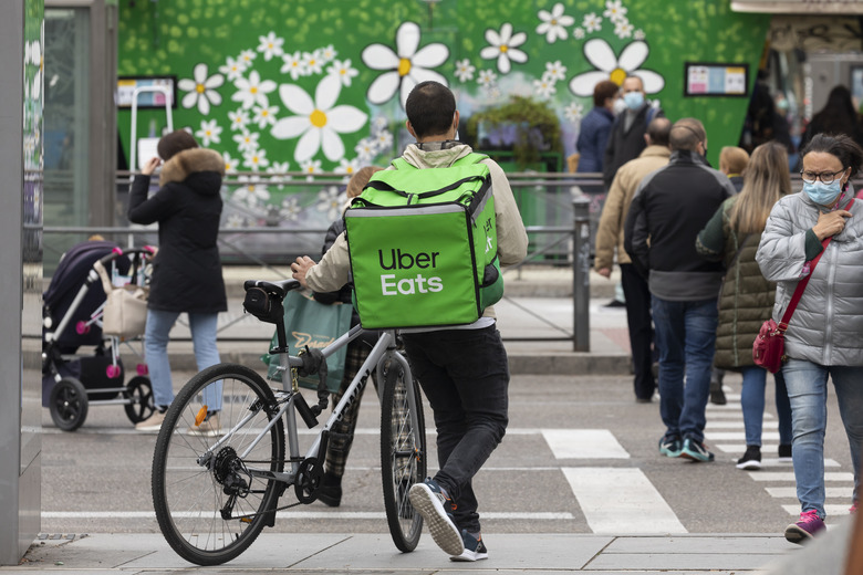 Madrid, Spain - Nov 25, 2020: A worker, a food delivery delivery man for the Uber Eats company, walks with his bicycle and crosses Narvaez street