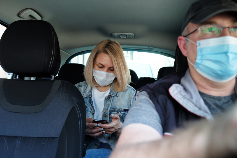 Caucasian woman in taxi wearing face mask for protection from pollution and viruses such as Coronavirus. Using smartphone