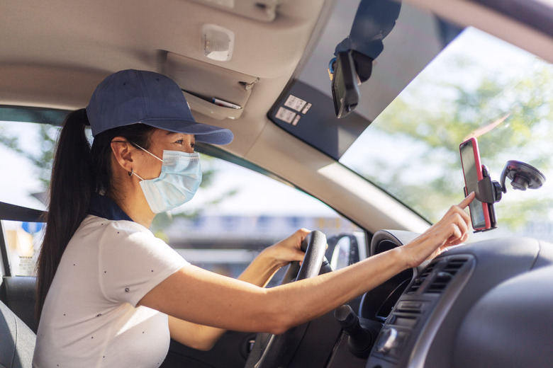 Asian female Car sharing driver checking on the mobilephone searching for job destination, woman wearing face mask while driving