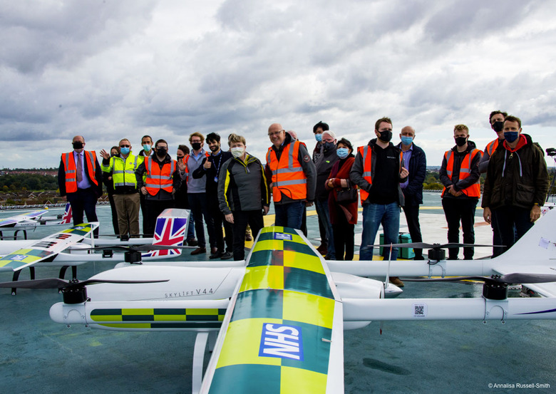Image of some officials standing around a drone while the NHS is incapable of offering a GPs appointment thanks to 12 years of chronic underfunding. 