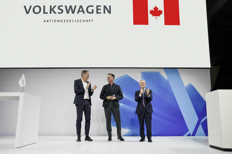 Volkswagen Group CEO Oliver Blume; Thomas Schmall, Group Board Member Technology; and Hon. François-Philippe Champagne, Canada’s Minister of Innovation, Science and Industry stand on stage in front of a screen displaying a Volkswagen logo and the Canadian flag.