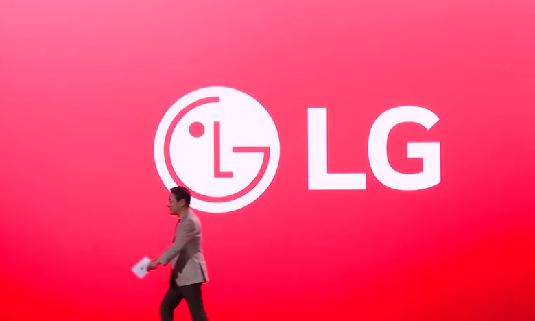 Screenshot of an LG executive walking to camera-left in front of an enormous screen showing an LG logo against a red background.