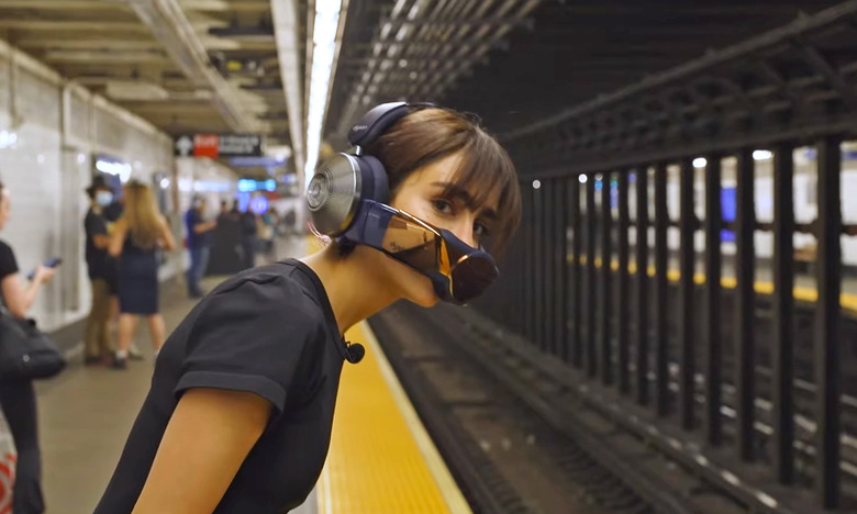 A young woman wearing the Dyson Zone headphones and breathing mask leans over the subway platform edge to see if a train is coming.