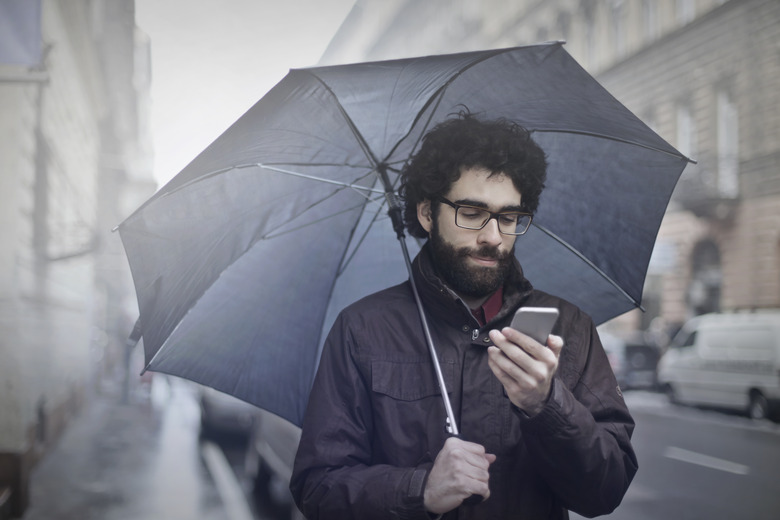 Man is walking on the street with an umbrella and his phone