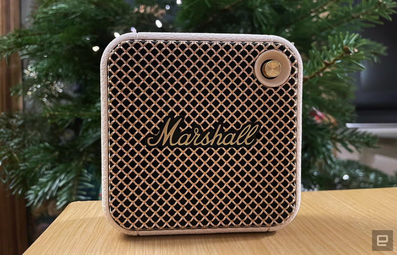A white Marshall Willen Bluetooth speaker sits on a table with a holiday tree in the background.