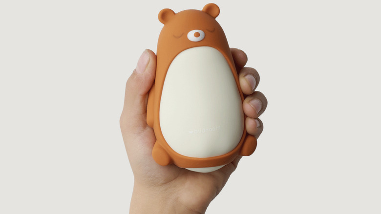 A hand holds the Moonbird Moonbuddy. The device has the teddy sleeve on.