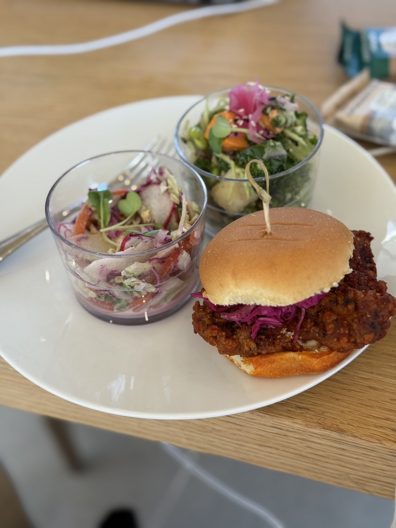 A plate on which a fried chicken slider and two cups of salads are sat.