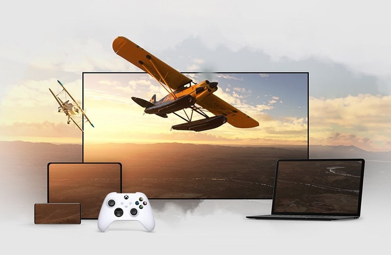 A white Xbox controller pictured in front of the Flight Simulator game shown on multiple displays, including a smartphone, tablet, laptop and large monitor