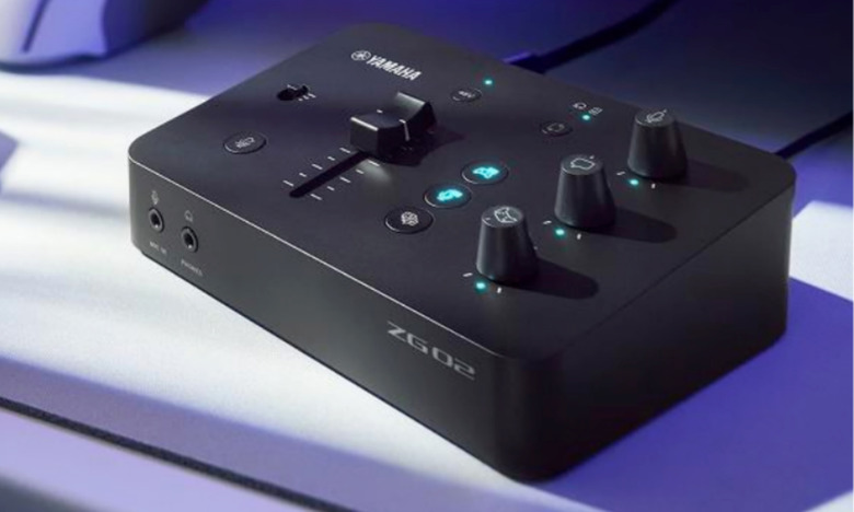 Product marketing photo of the Yamaha ZG02 mixing board for gamers. The black device has knobs, a slider and buttons. It sits on a purple surface with scattered sunlight.