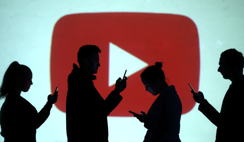Silhouettes of mobile users are seen next to a screen projection of Youtube logo in this picture illustration taken March 28, 2018.  REUTERS/Dado Ruvic/Illustration