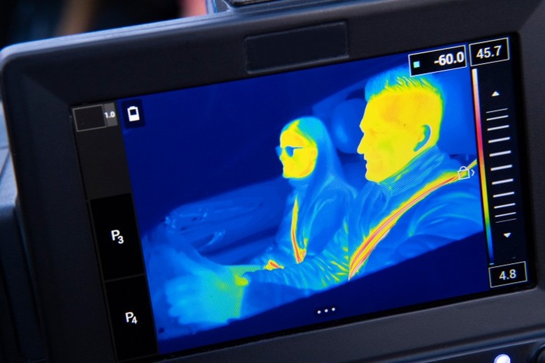 thermal camera view of two people pretending to drive a car while their seatbelts burn stripes in thier torsos