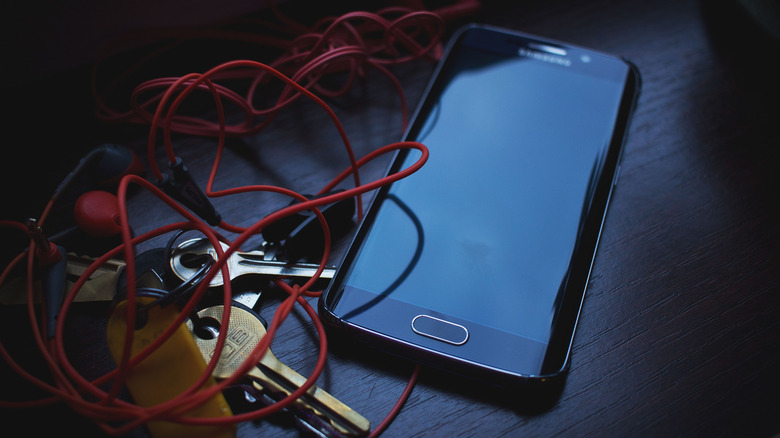Close-up of a smartphone, red earphones, and keys slightly jumbled.