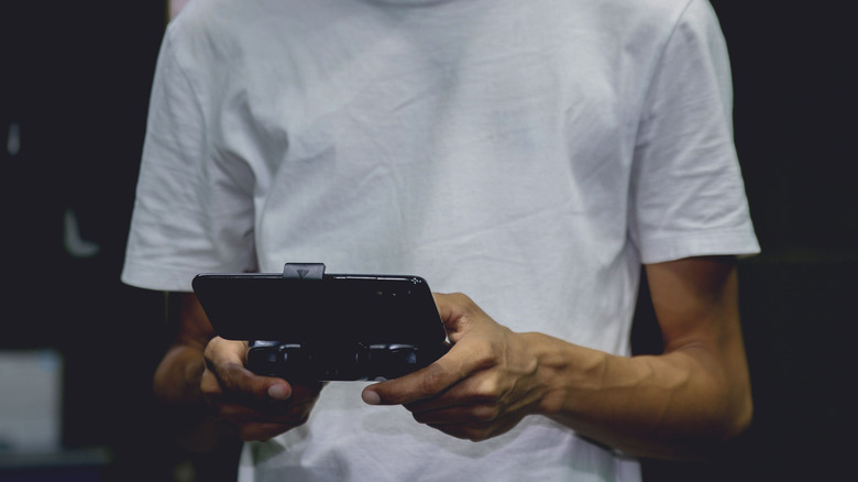 A young man in a white shirt using a smartphone game controller indoors.