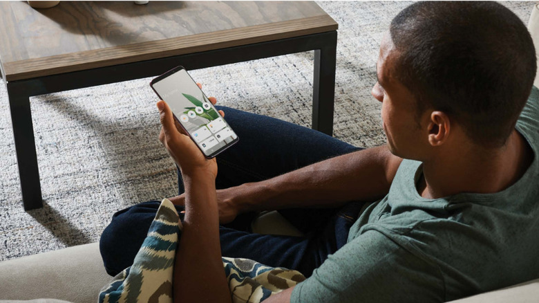 Person sitting on couch using old Android phone as dedicated smart-home control panel.