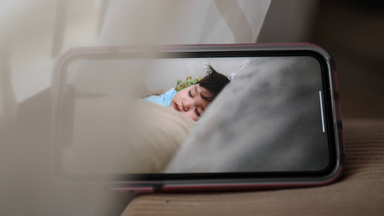 A smartphone displaying a sleeping baby in a cozy, indoor setting, conveying warmth and care.