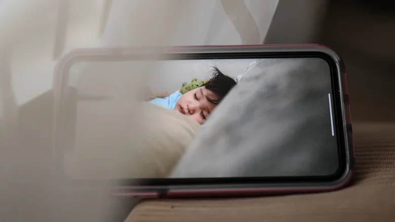 A smartphone displaying a sleeping baby in a cozy, indoor setting, conveying warmth and care.