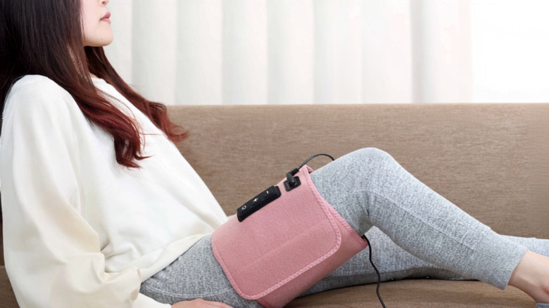 Woman laying on couch using a pink Gorilla's Two Grips Massager on her thigh.