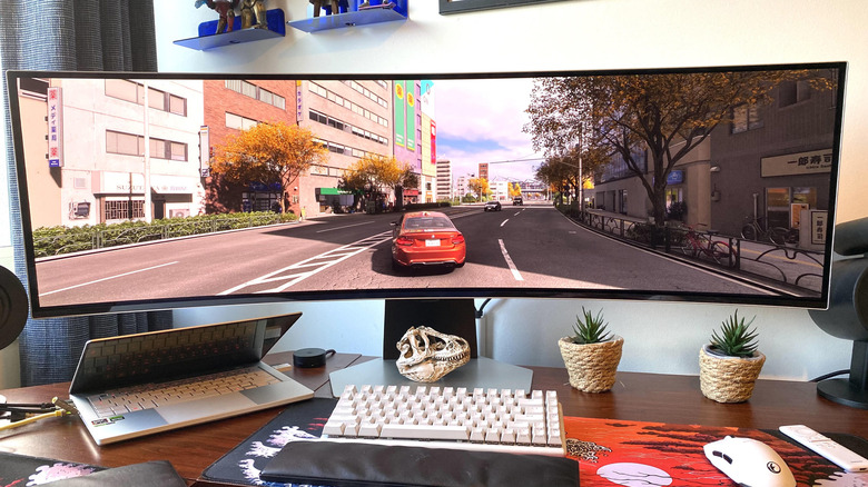 A red car driving through Tokyo in Forza Horizon 6 being played on a gaming laptop connected to a super ultrawide monitor.