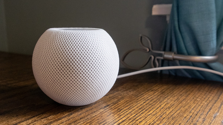 A white HomePod mini speaker sitting on a wooden desk.