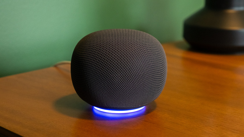 A black Google Home speaker sitting on a desk with its light ring activated.