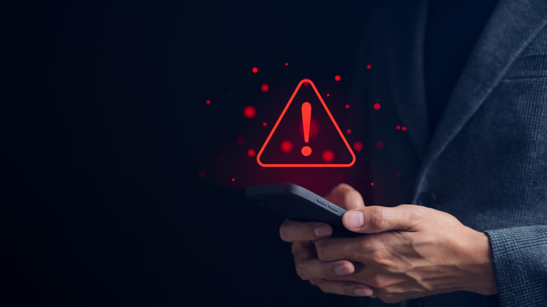 Person holding smartphone with triangle caution warning sign
