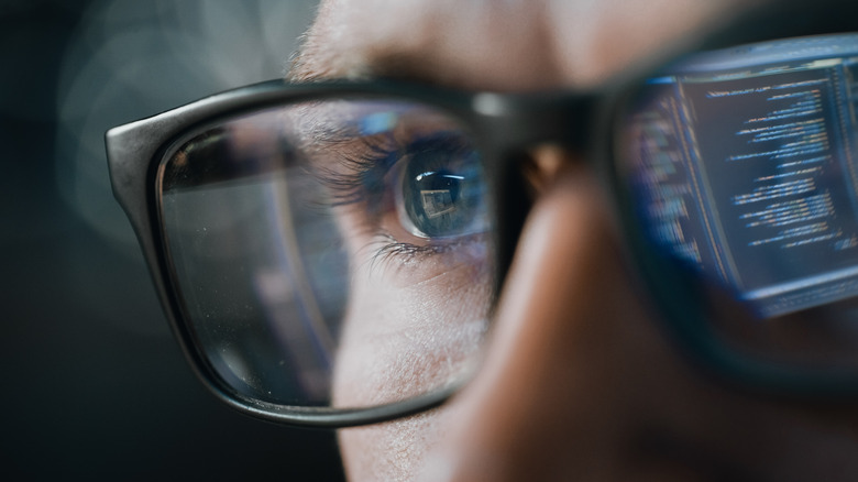 A close-up shot of computer code reflected in a person's glasses.
