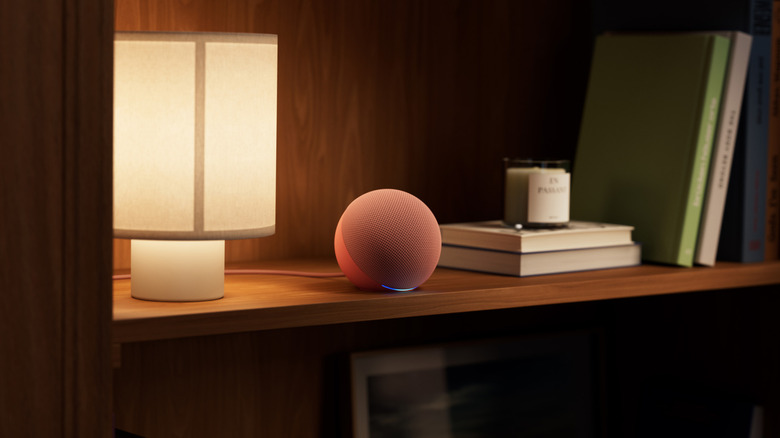 Amazon Dot speaker shown on a bookshelf with a fancy candle on one side and white lamp on the other
