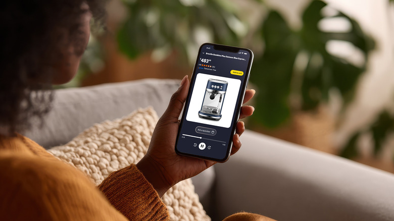 Over-the-shoulder view of a person holding a phone. The Amazon shopping app is playing an AI "Hear the highlights" product recap.